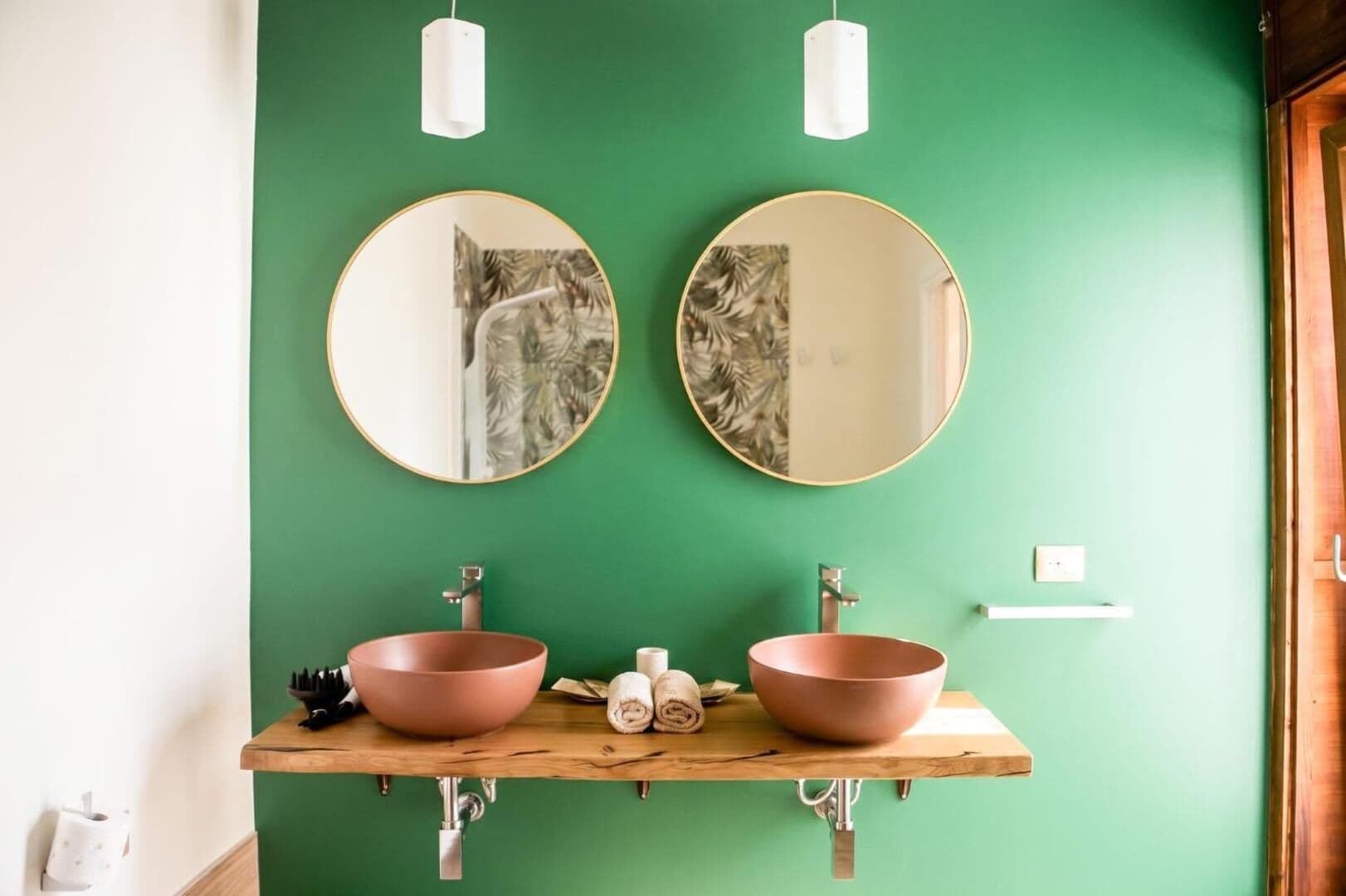 Il bagno verde con i due lavabi in ceramica rosa e gli specchi tondi